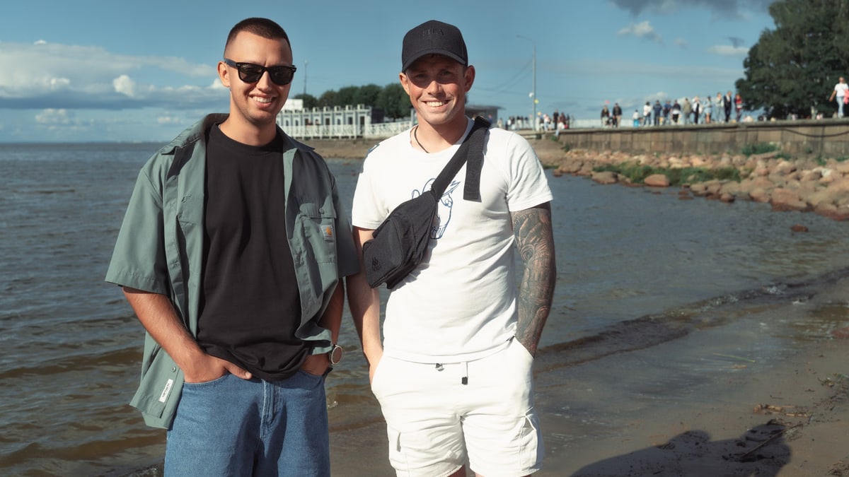 Two young men smiling near the sea on a sunny day, enjoying the beach atmosphere.